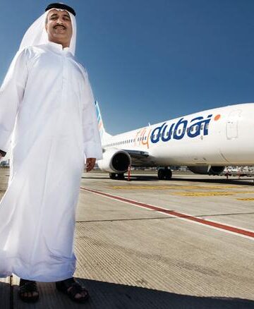 a man in a white robe with a suitcase standing in front of an airplane