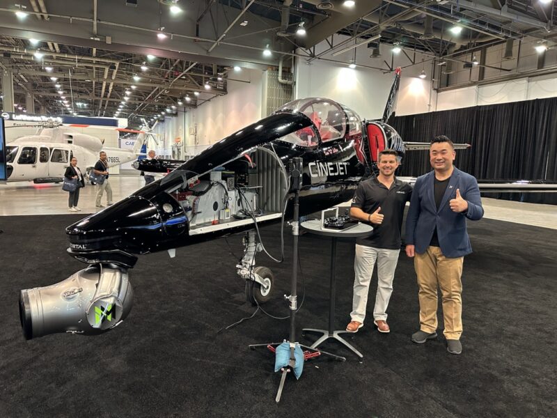 two men standing next to a black and silver airplane