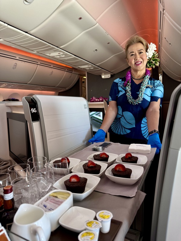 a woman standing in a plane with trays of desserts