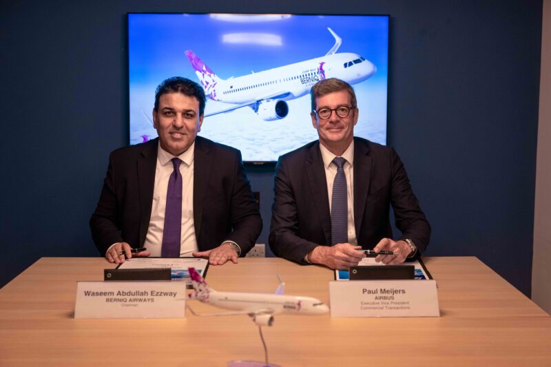 two men sitting at a table with signs and a plane on it