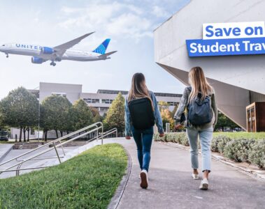 two women walking on a sidewalk with a plane flying in the sky